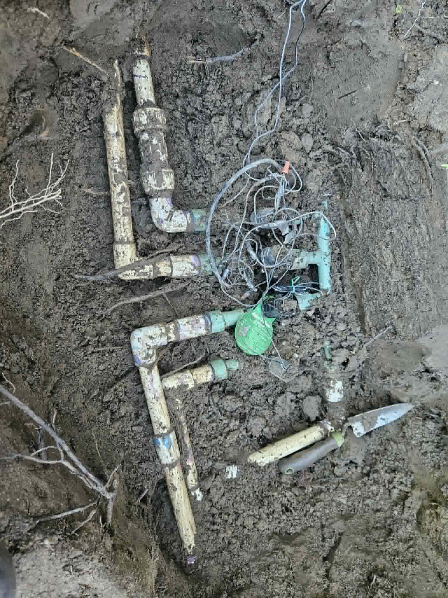 Step one of an irrigation manifold rebuild showing an old buried valve manifold with exposed PVC pipes and tangled wires