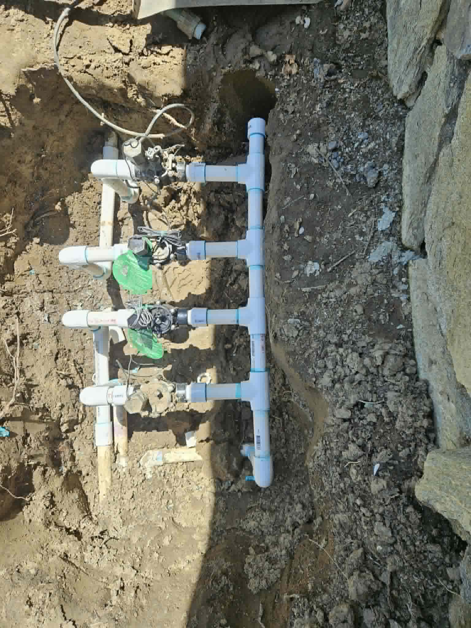 Step three of an irrigation manifold rebuild showing a new PVC manifold with multiple sprinkler valves reconnected in the trench